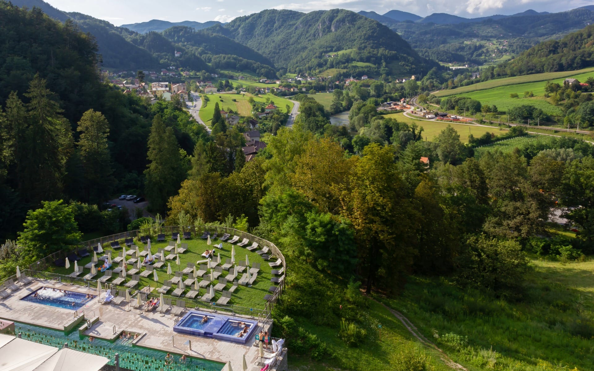 Aerial view of a thermal spa resort with outdoor pools and loungers among green grounds