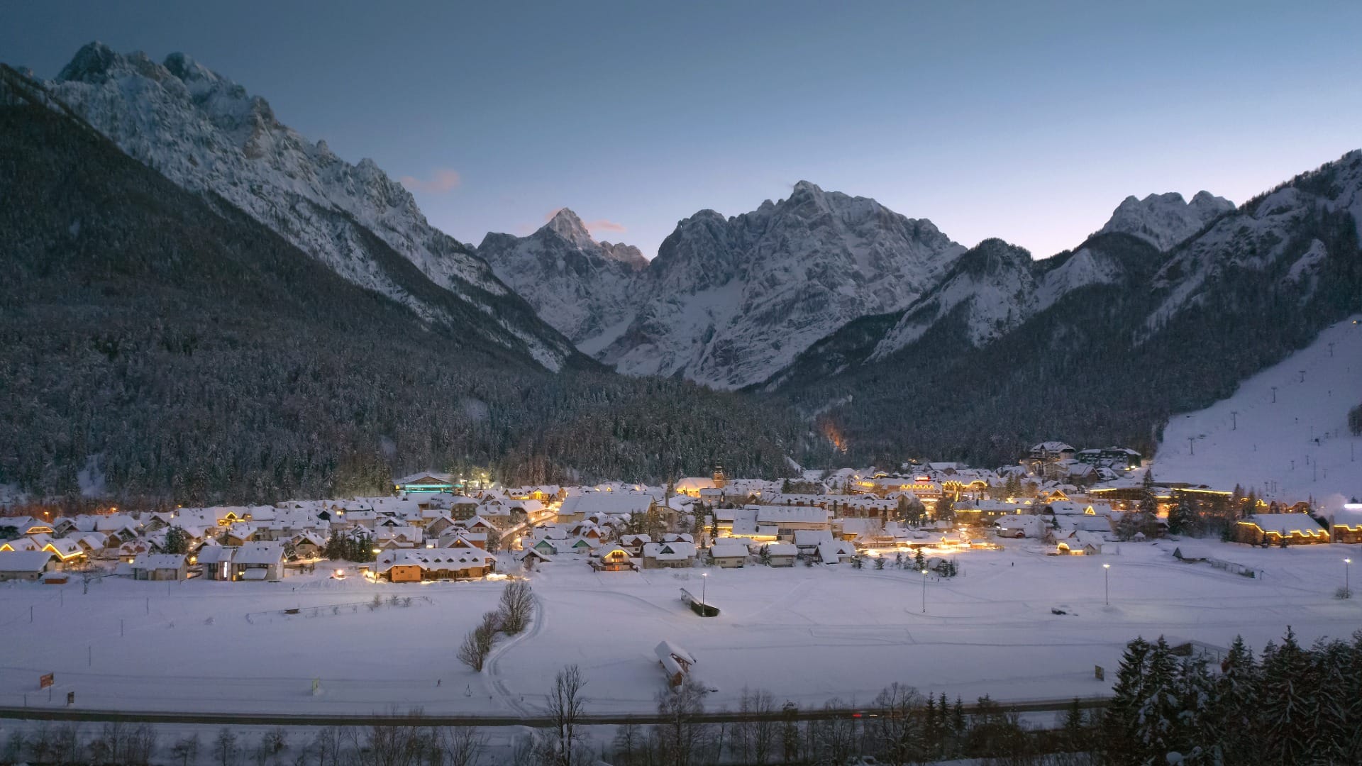 Kranjska Gora village lit up at dusk with the Julian Alps and a lit ski slope behind it