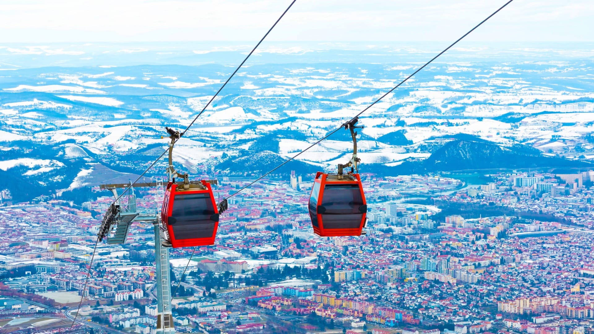 Red gondola cabins descending toward a city at dusk, similar to the Pohorje cable car above Maribor