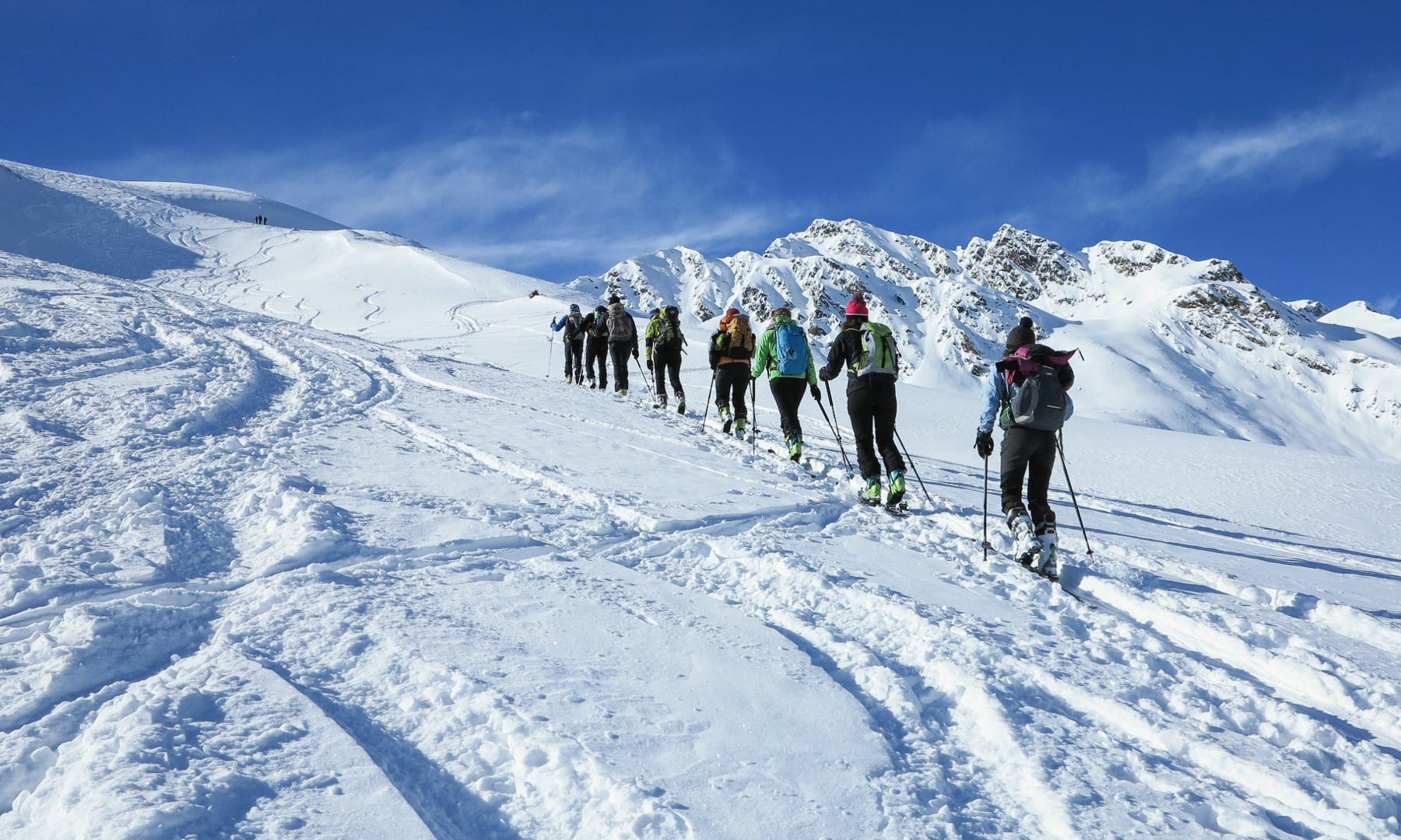 Line of backcountry ski-tourers with skins ascending a snowy ridge