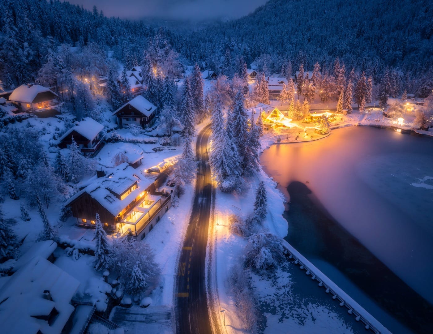 Aerial night view of a road leading to a small, warmly lit Slovenian town in winter