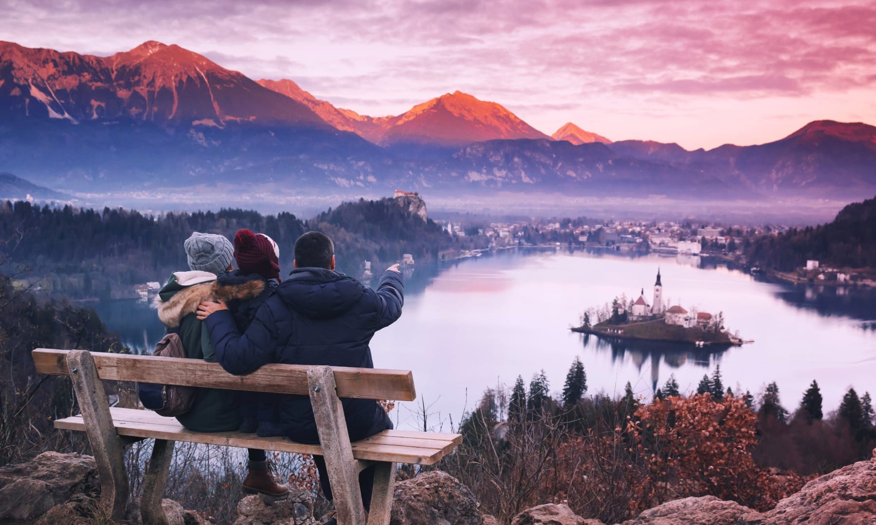 Couple and child sitting on a bench overlooking Lake Bled and its island at sunset