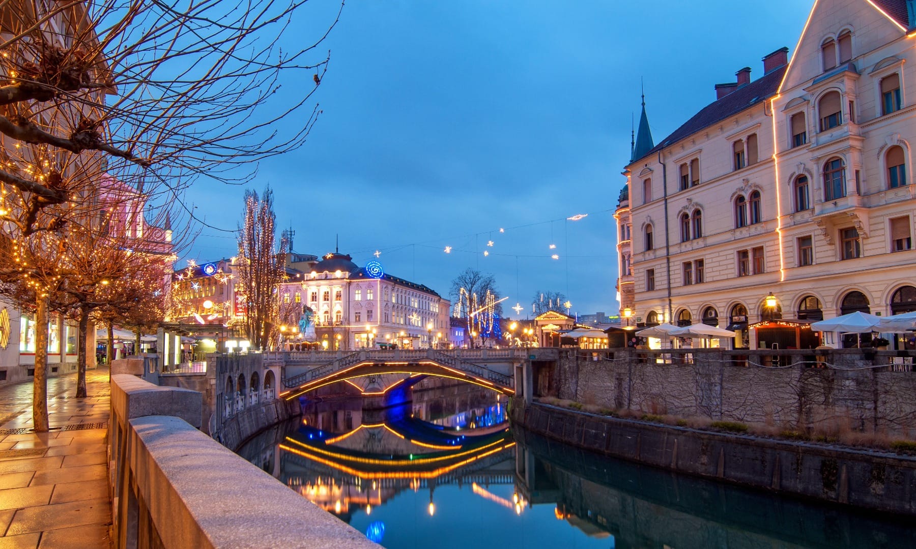 Ljubljana's riverside canal and bridge lit up for Christmas at dusk
