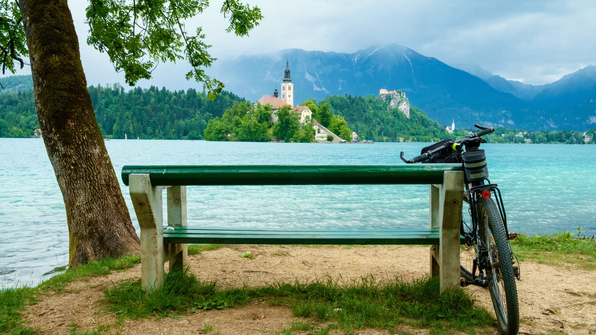 Bicycle parked by a lakeside bench at Lake Bled, with the island church and Bled Castle visible
