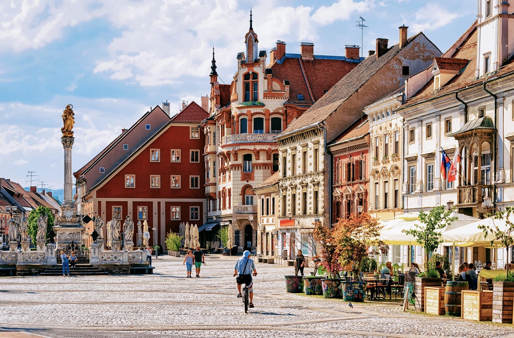 Maribor's main square with the baroque plague column and town hall, a cyclist crossing the cobbles