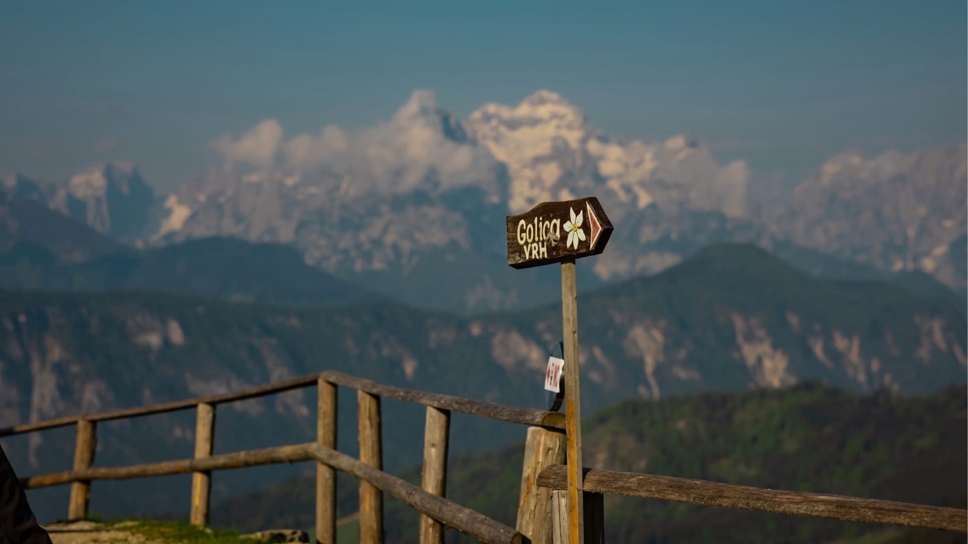 Golica VRH summit signpost with the snow-capped Julian Alps in the background