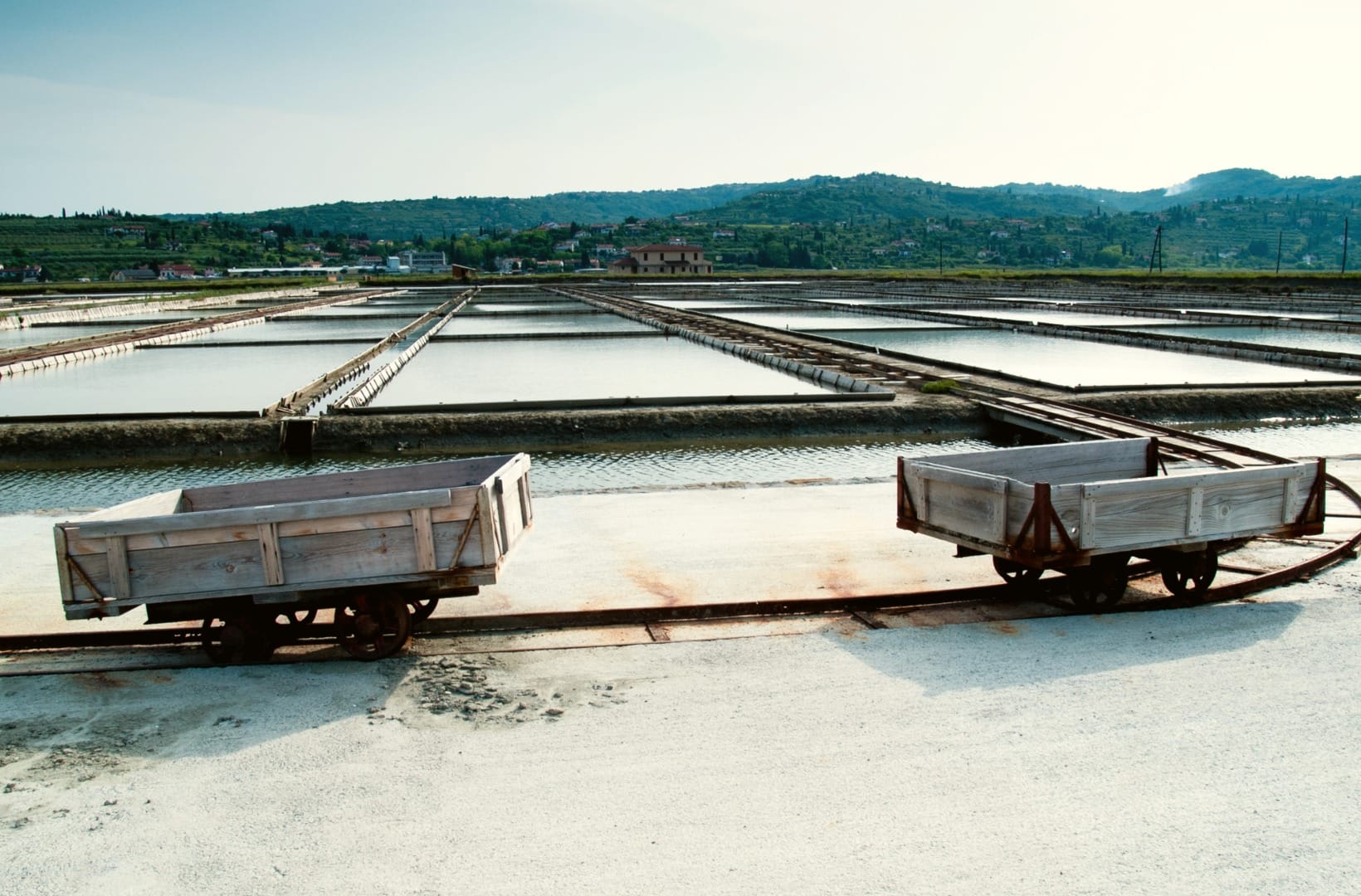Old wooden narrow-gauge wagons on rails beside the flooded evaporation basins of the Sečovlje salt pans