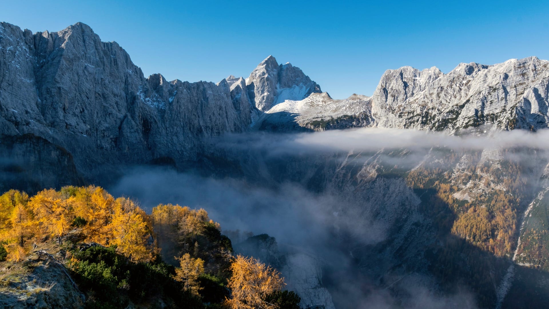 Cloud inversion filling the valley below snow-capped Julian Alps peaks, seen from Slemenova Špica