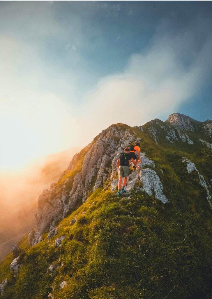 Two hikers on a misty mountain ridge at golden hour, Slovenia
