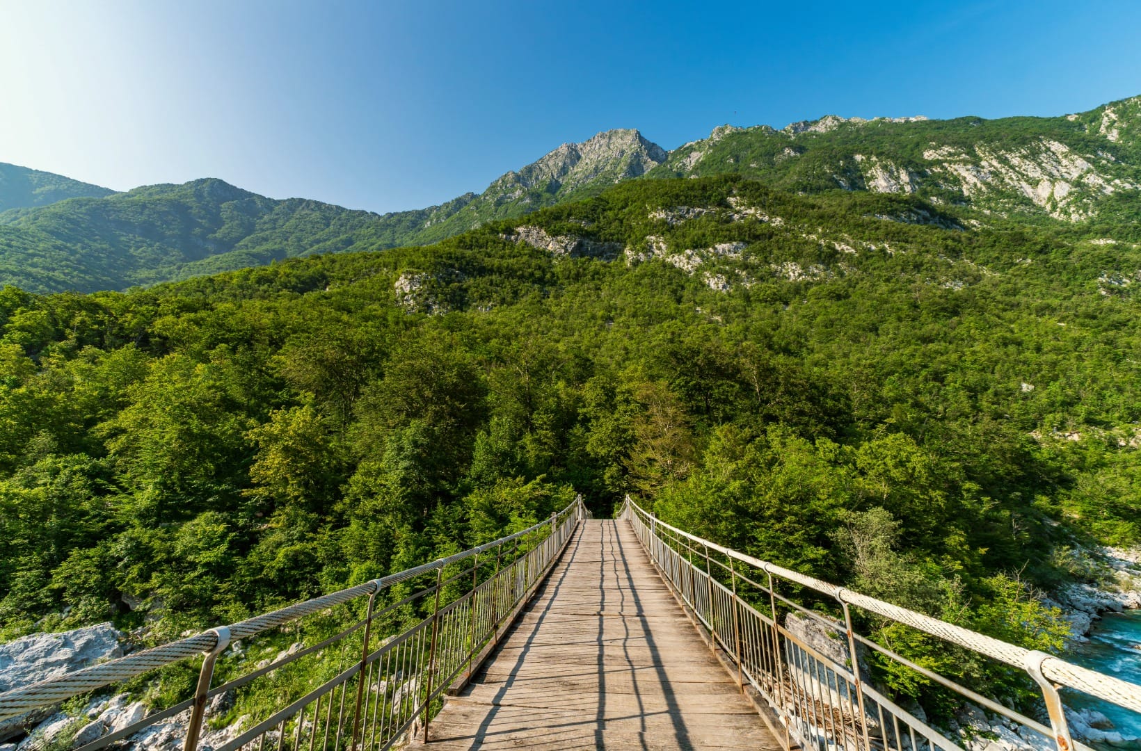 A narrow wooden suspension footbridge on cables spanning the forested Soča gorge