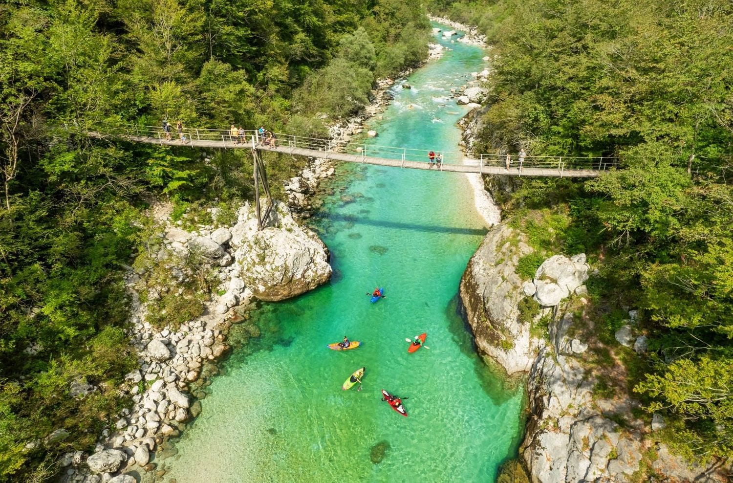 Aerial view of the wooden suspension footbridge over the Great Soča Gorge with kayakers on the turquoise pool below