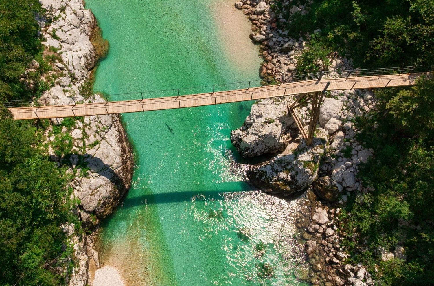 Long wooden suspension bridge spanning the emerald Soča between forested banks near the Great Soča Gorge
