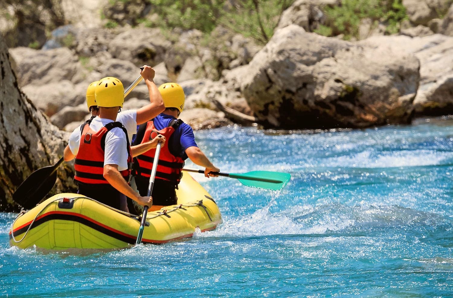 Two people in helmets and life jackets paddling a yellow inflatable kayak on the bright blue Soča