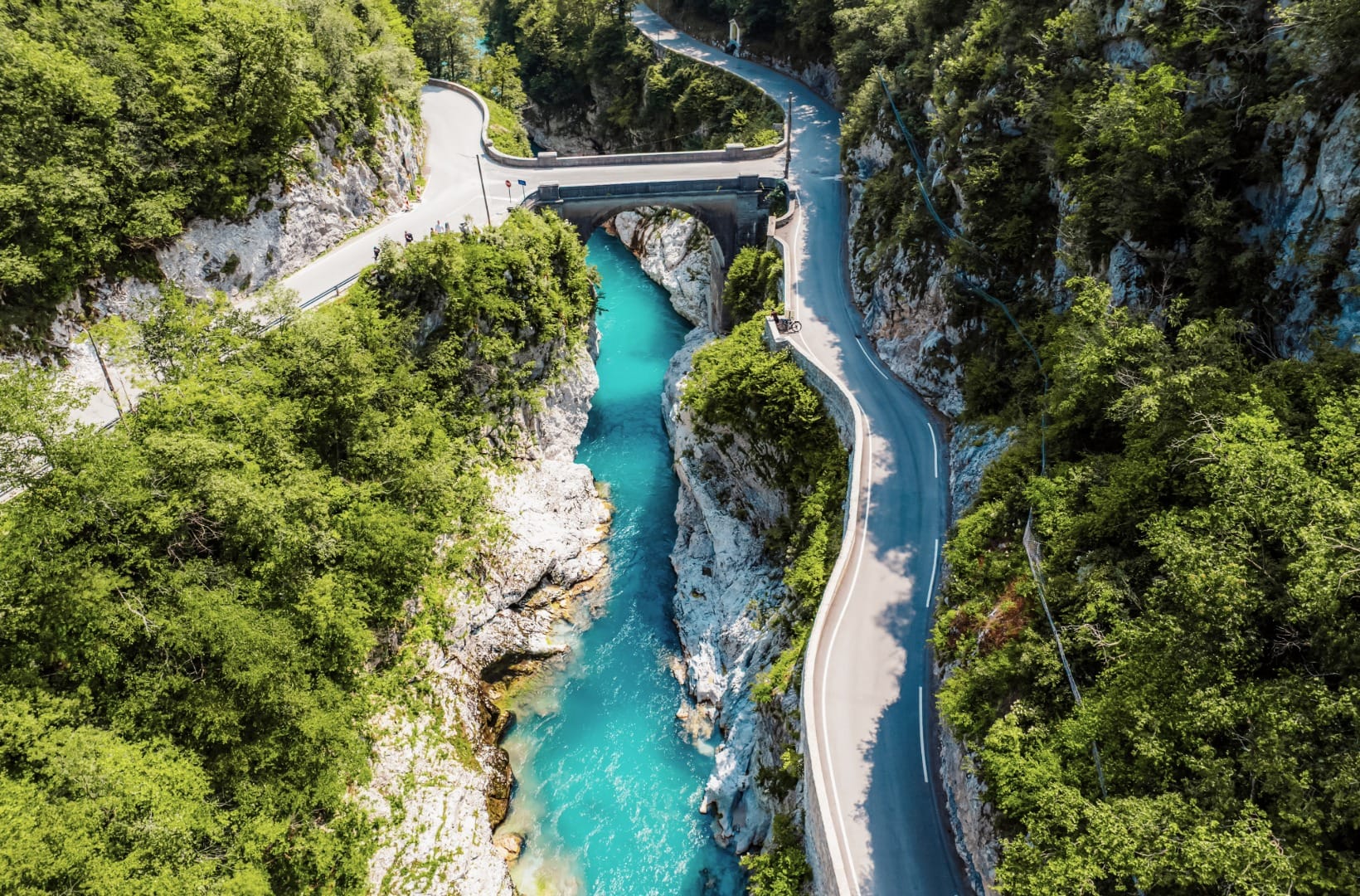 Aerial view of the stone Napoleon Bridge arching over the narrow emerald Soča gorge at Kobarid, a bike leaning on the parapet