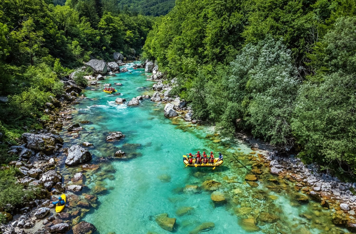 Aerial view of a raft and a kayak dropping through boulder rapids on the clear turquoise Soča