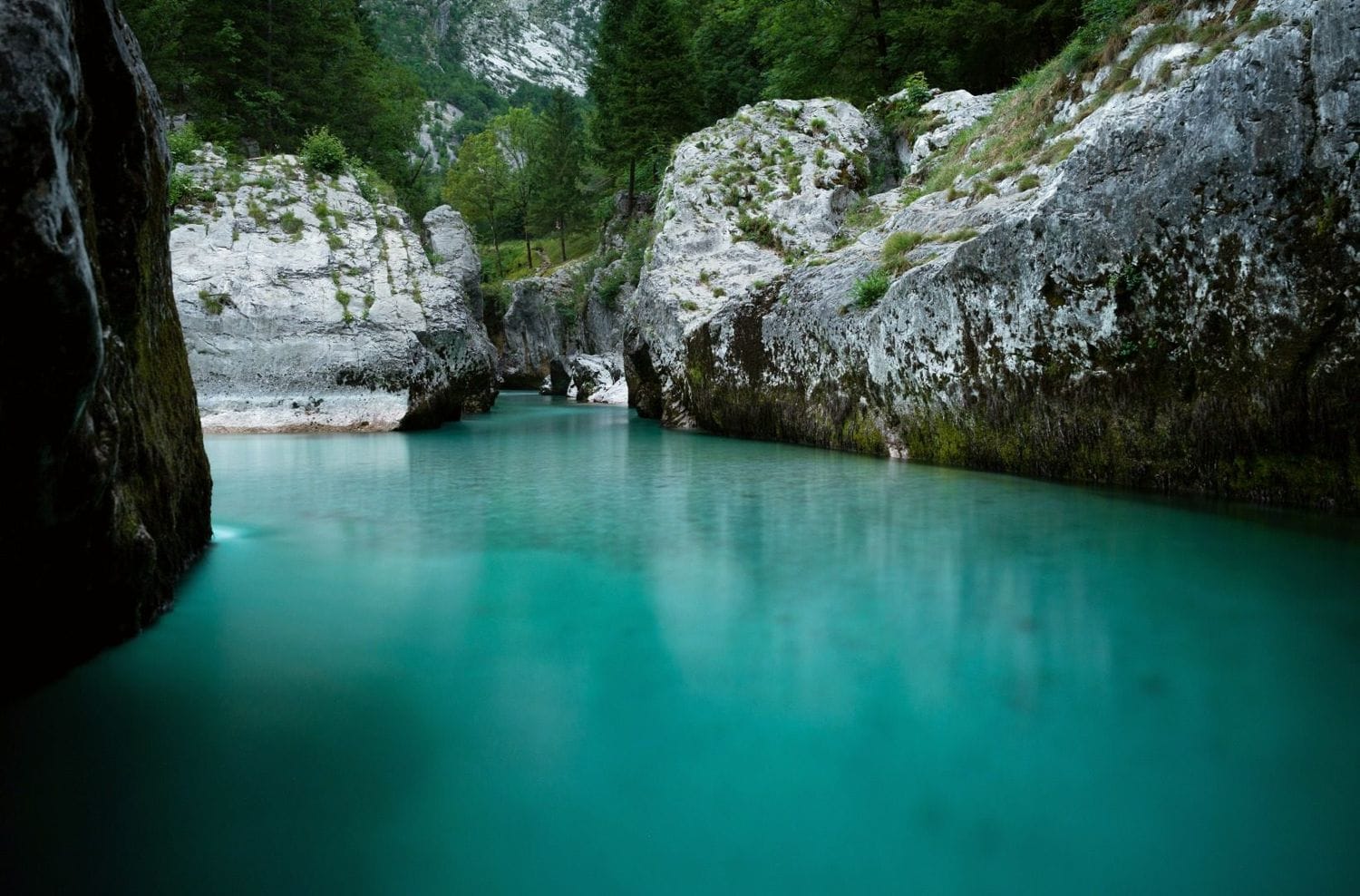 Wide calm turquoise pool of the Soča between low white rock ledges, a common swimming spot below the Great Soča Gorge