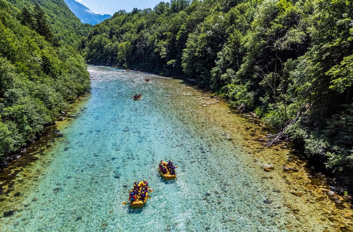 Aerial view of two yellow rafts drifting a wide, shallow, very clear stretch of the Soča between wooded slopes