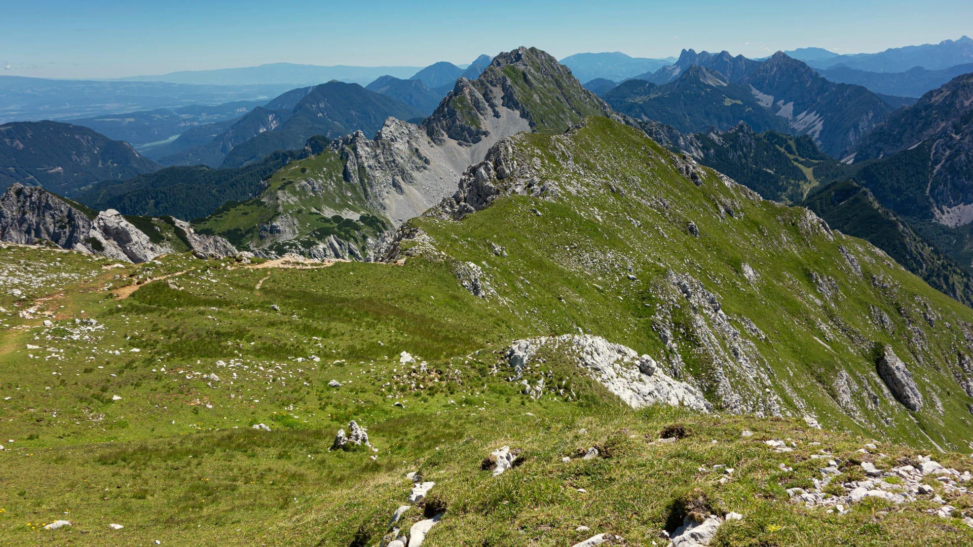 Wide green summit ridge of Stol with the Karavanke and Julian Alps stretching into the distance