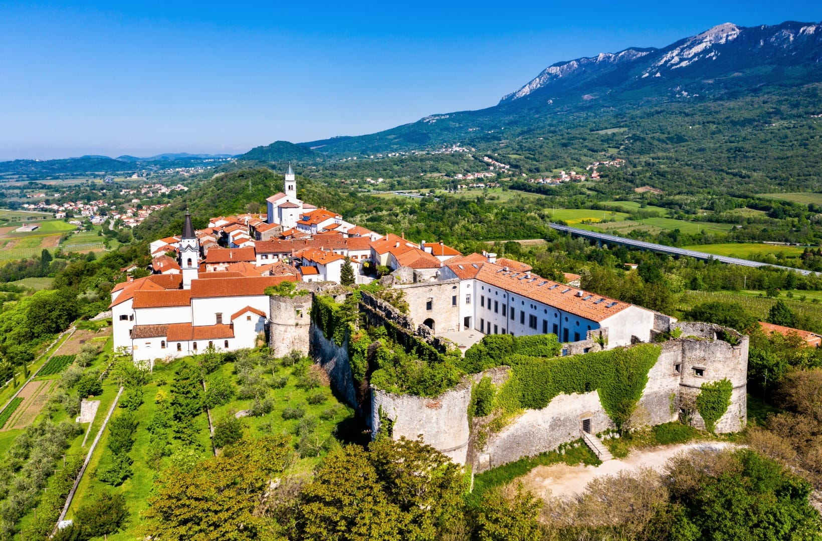 Aerial view of the fortified hilltop village of Vipavski Križ with its walls and monastery, the Nanos massif rising behind