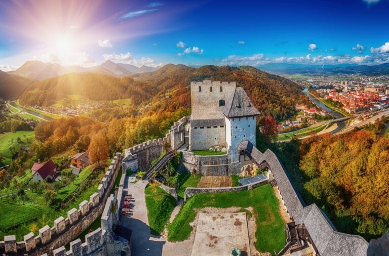 Aerial view from Celje Old Castle over the keep and walls, the Savinja river winding below, the town and autumn-coloured hills beyond