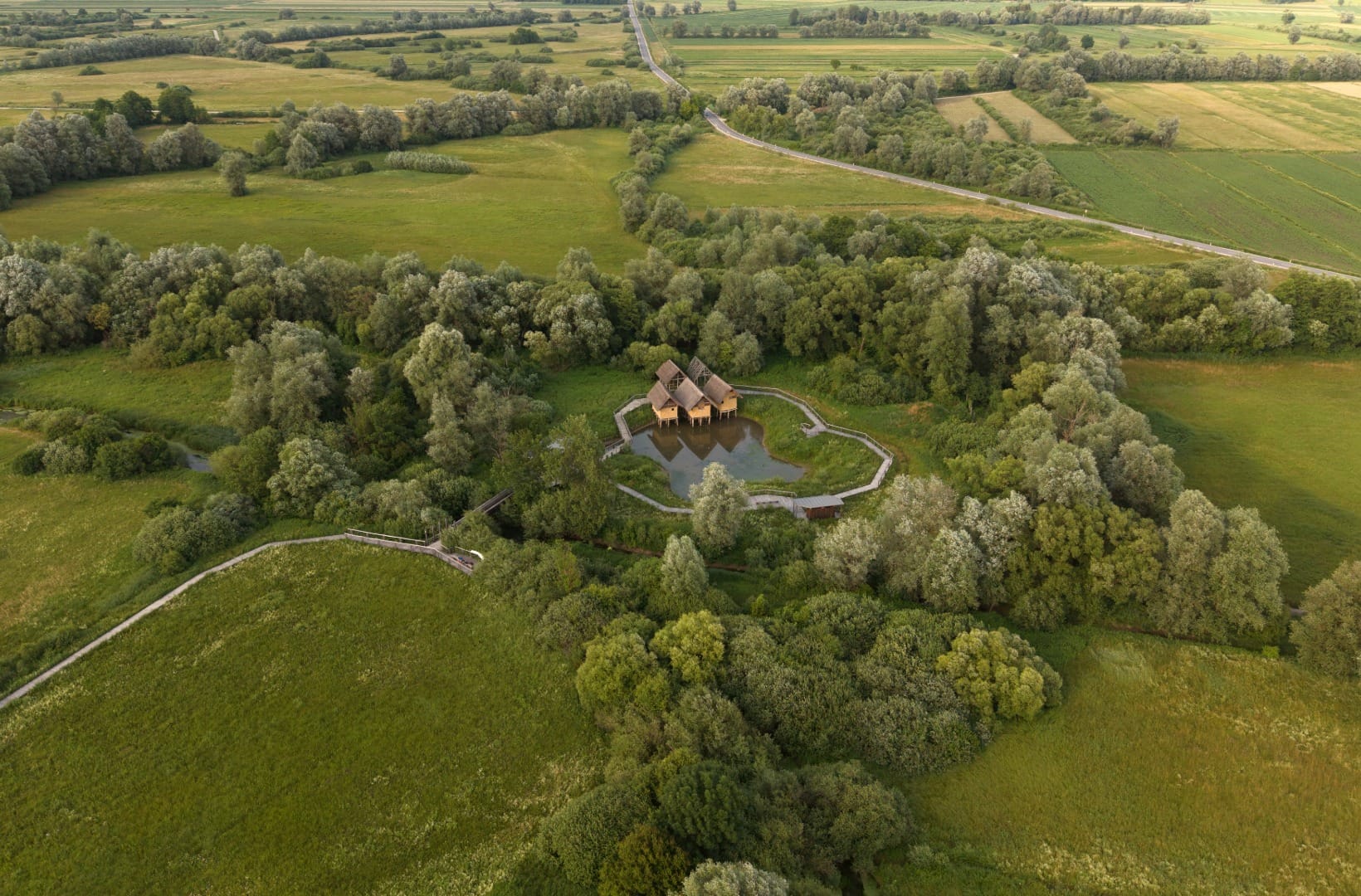 Aerial view of a reconstructed prehistoric pile-dwelling settlement on a small pond in the Ljubljana Marshes, ringed by a boardwalk