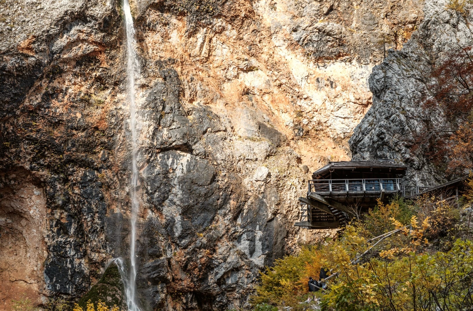The Rinka Waterfall beside the wooden Orlovo gnezdo café perched on a ledge on the cliff face, autumn colour
