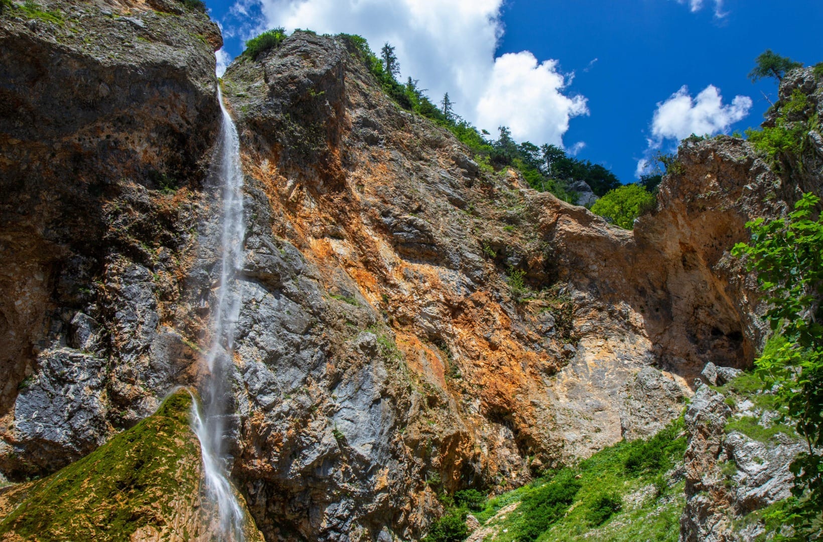 The Rinka Waterfall dropping in a thin white ribbon down a colourful orange and grey limestone cliff at the head of Logarska dolina