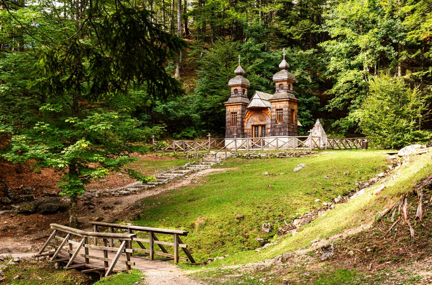 The wooden Russian Chapel on the north side of Vršič with two shingled onion-dome towers and Orthodox crosses, a small footbridge in front