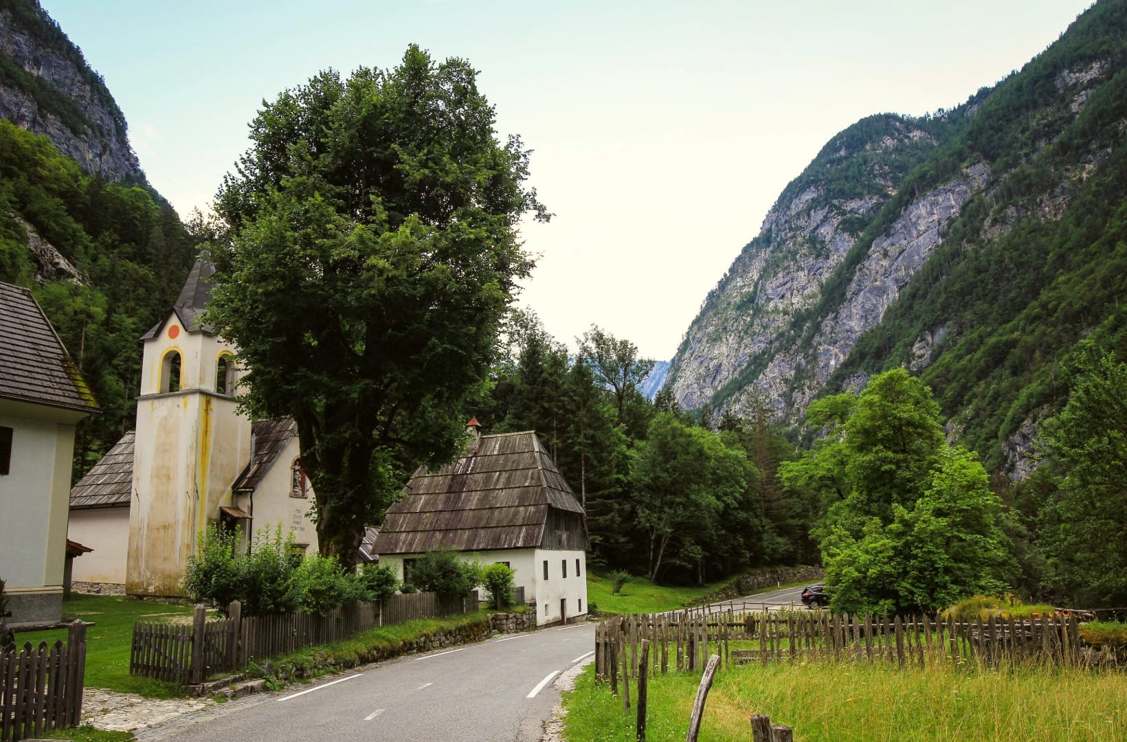 A small pastel-towered church and shingle-roofed houses in the hamlet of Soča, hemmed in by high grey cliffs on both sides