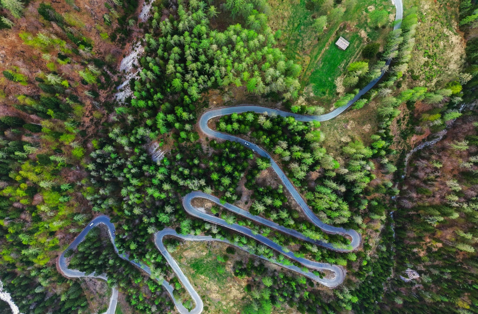 Aerial view of the Vršič road folding back on itself in tight hairpins through dense forest